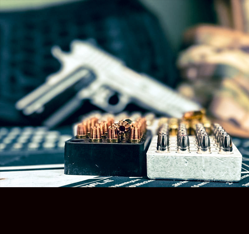 Two boxes of ammo sitting in front of a 1911 pistol. 
