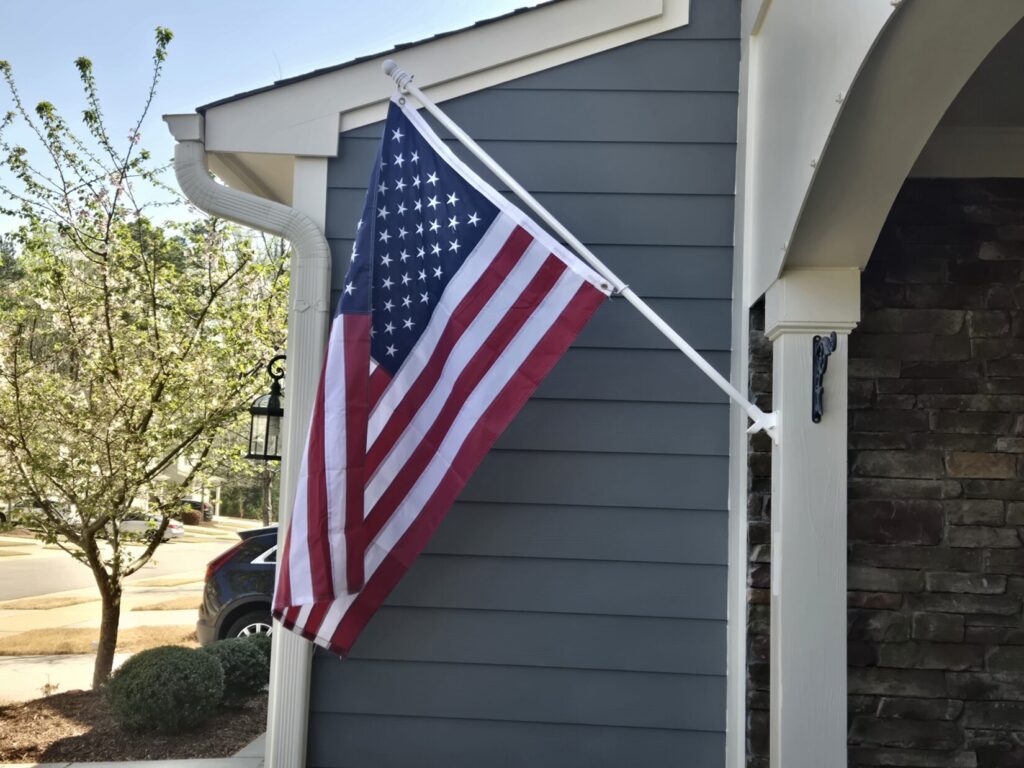 An American flag hanging on a flag pole outside of a house