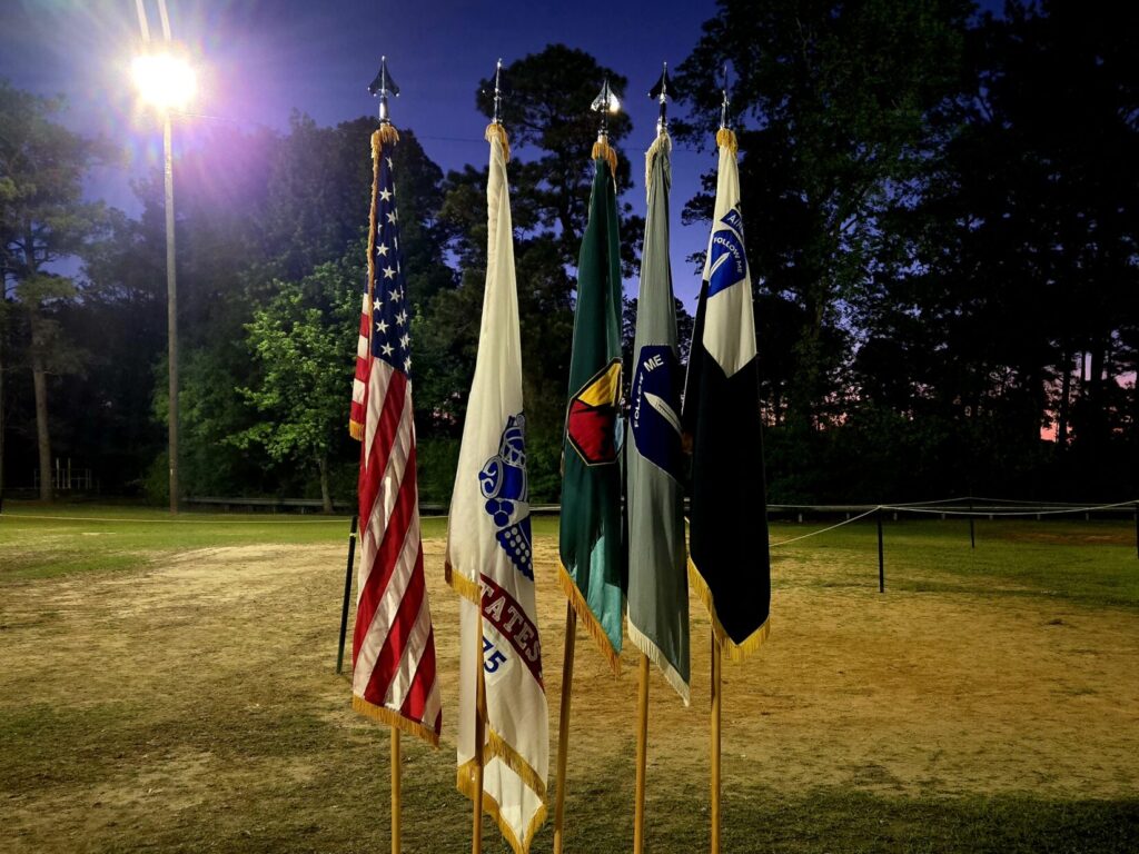 Multiple flags on a display with a light on them and trees in the background