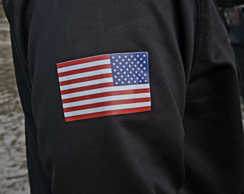 A man in a black sweatshirt with the American flag on his right sleeve