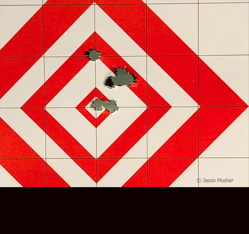 A red and white target with bullet holes, above and to the right of the center, and two holes in the center.