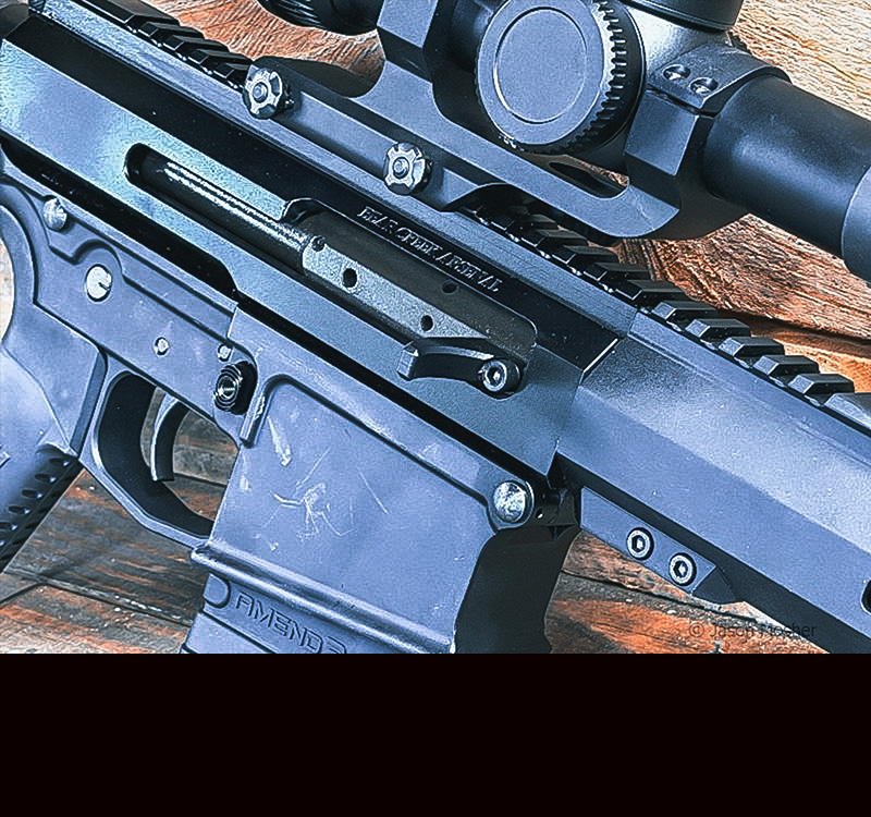 A view of the side of a BCA AR-10 rifle, showing the charging handle mounted directly to the bolt of the gun.