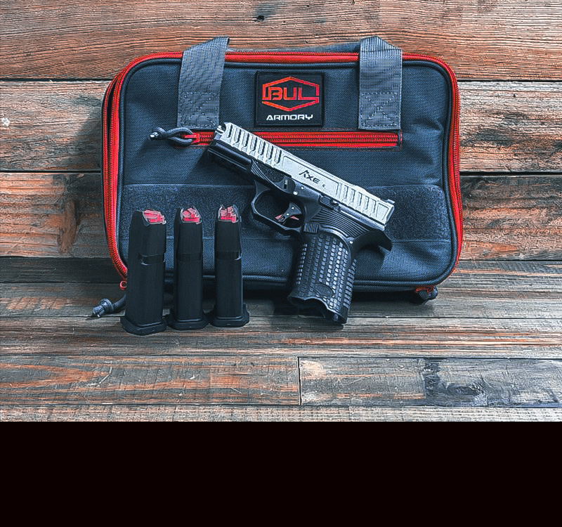 A black and silver handgun, and three magazines in front of a red and black gun case. 