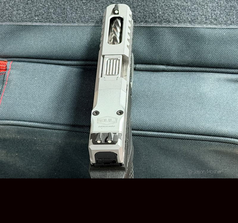 The top of a silver slide on a AXE handgun, showing the barrel through the cutout on the slide. 