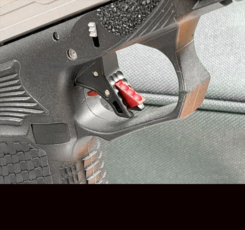 A close up view of the trigger on a Bull Armory AXE Tomahawk c handgun, showing the red trigger safety. 