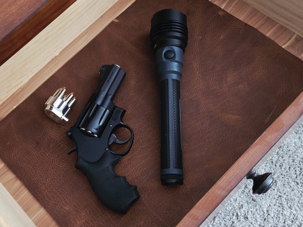 A speed loader, revolver, and flashlight inside of a night stand.