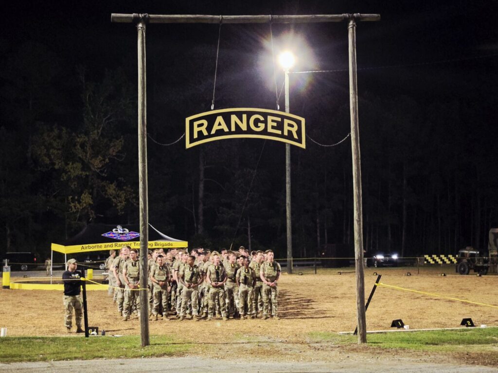 Soldiers stand in a field with a ranger sign overhead