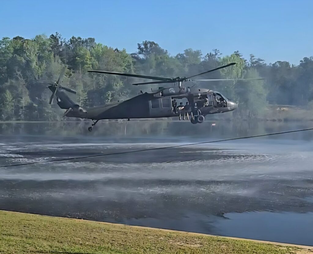 A helicopter flies low over a pond with men seated in the doorway