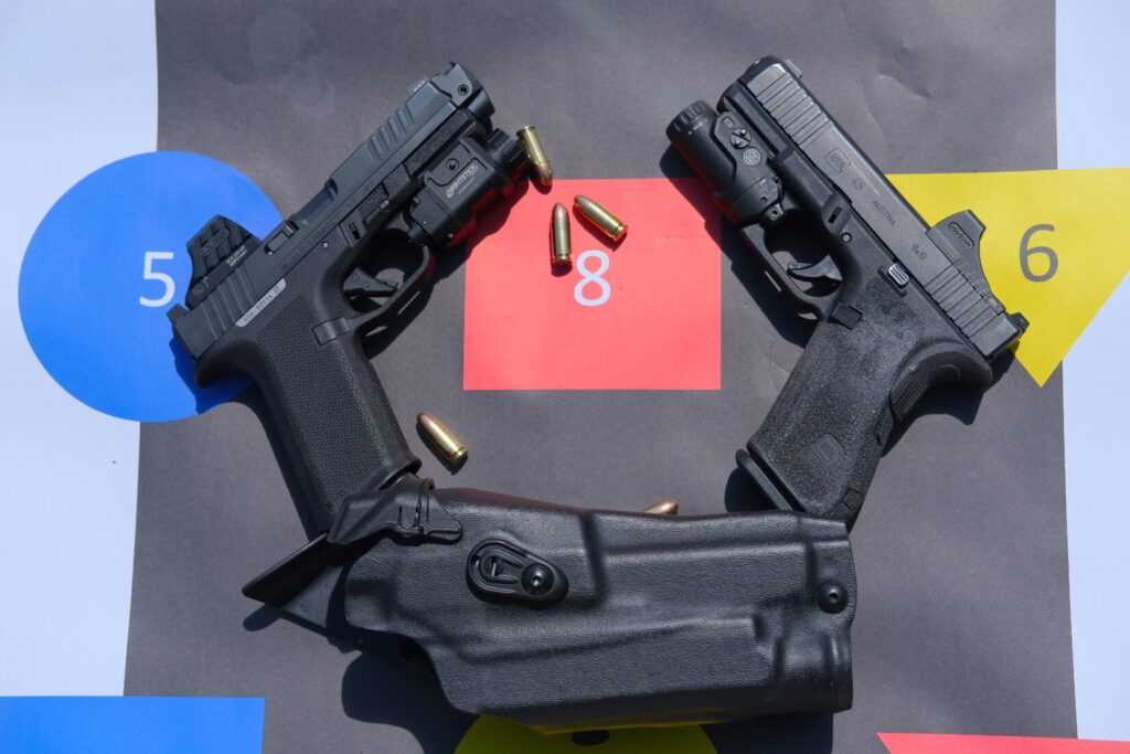 A black, compensated Ruger RXM with an optic and weapon light, a Gen 5 Glcok 45 with an optic and weapon light, a black Safariland 6390 holster on an RTG target with some loose 9mm rounds