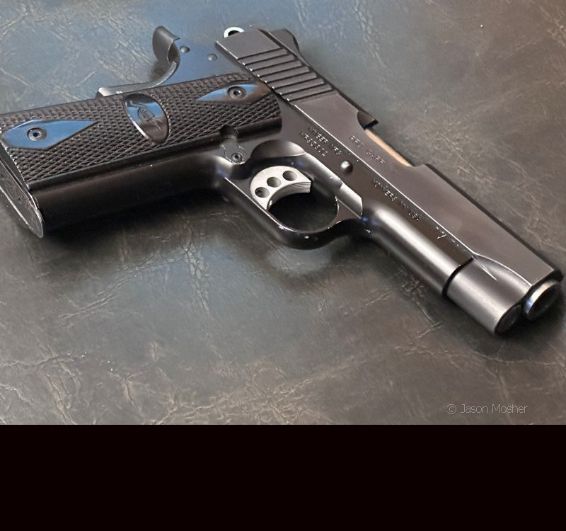 A black 1911 handgun laying on a dark leather chair. 