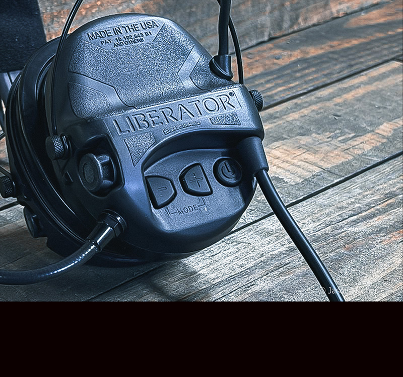A black headset on a wood table, showing the larger buttons on the side of the Liberator headset.