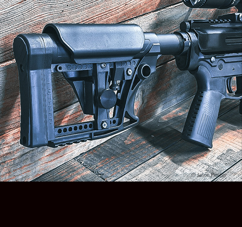 A black plastic stock on a rifle, leaning up against a wood table.