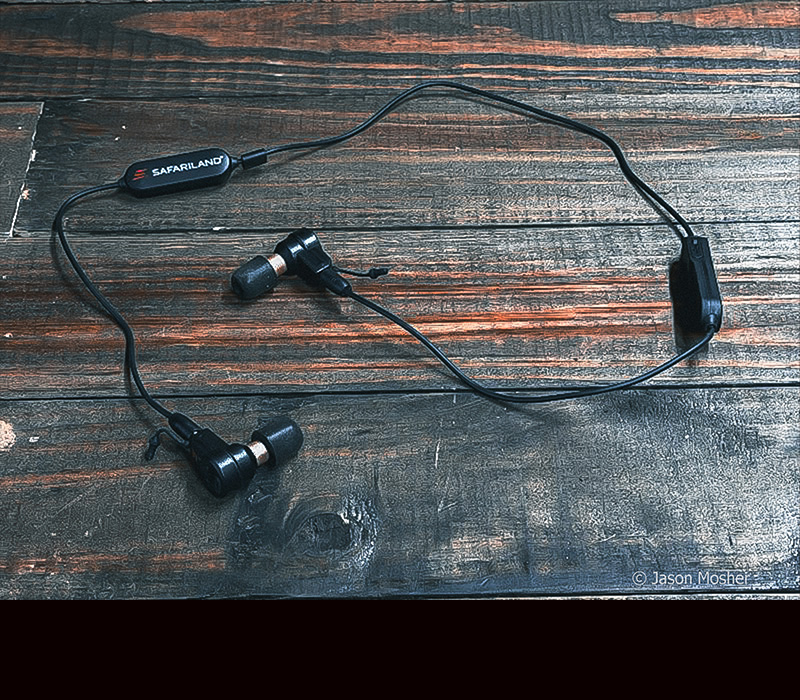 A pair of black ear buds connected to a lanyard laying on a wood table.