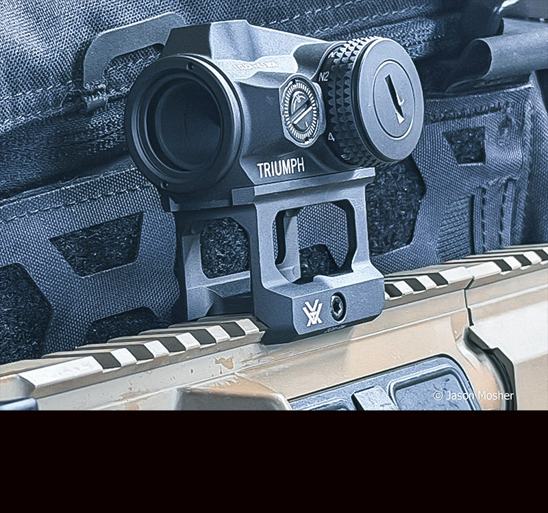 A view of the Triumph red dot, showing the red dot mounted to a picatinny rail. 