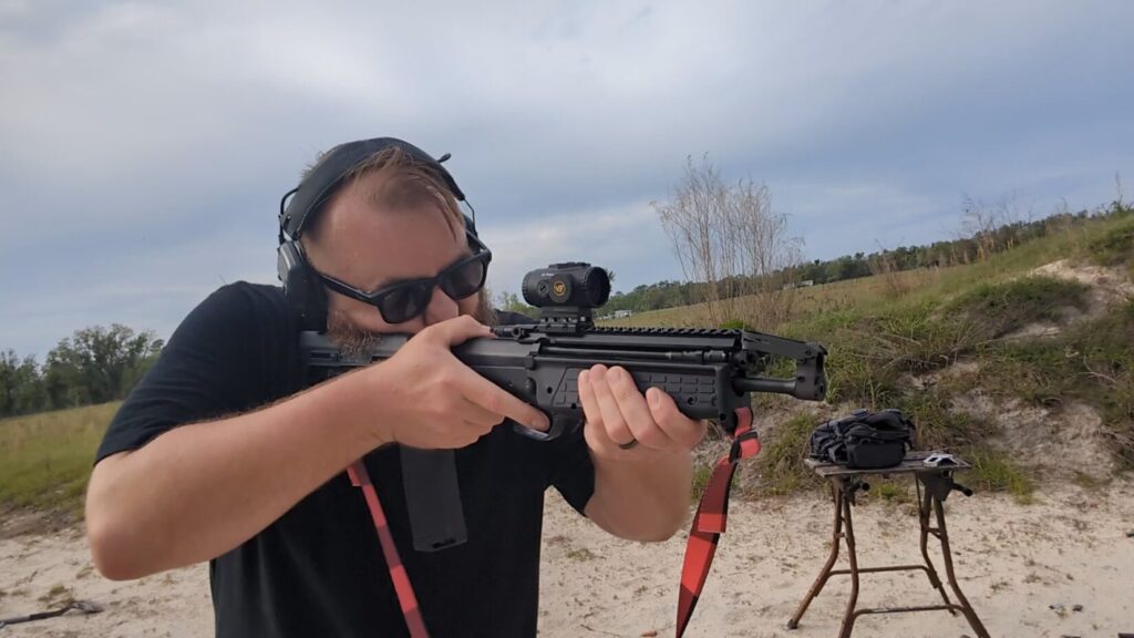 A head-on shot of the shooter aiming the RDB-S, highlighting the slim handguard and the red buffalo check sling.