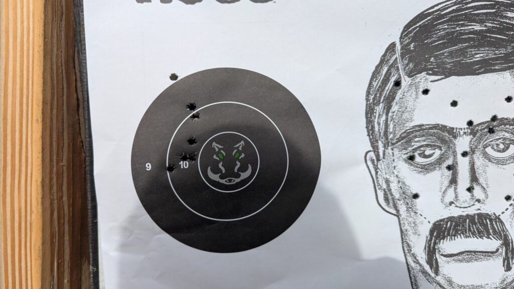 A paper shooting target showing several hits on a humanoid silhouette and a circular bullseye.