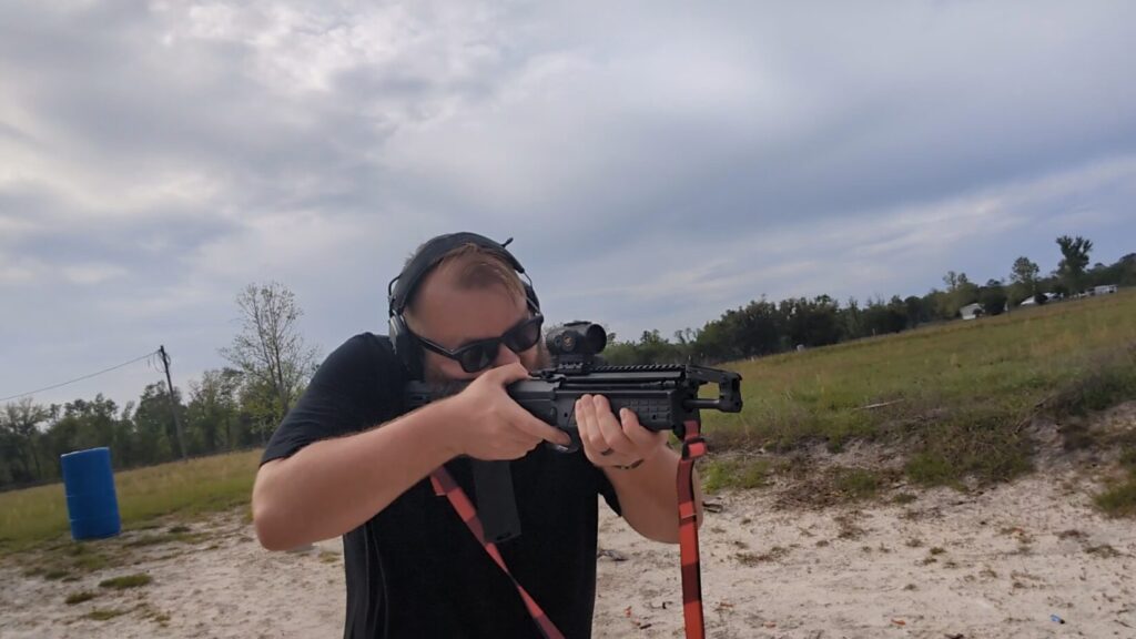A shooter firing the RDB-S at an outdoor range, with the action cycled and an empty casing visible on the blue barrel.