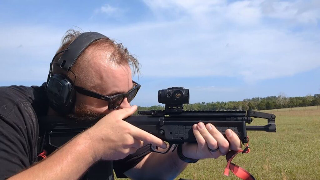 A head-on shot of the shooter aiming the RDB-S, highlighting the slim handguard and the red buffalo check sling.