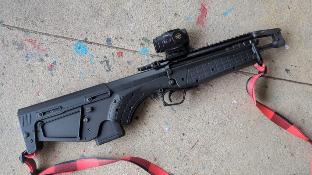 A top-down view of the RDB-S resting on a grey concrete surface, showing the folding iron sights and mounted optic.