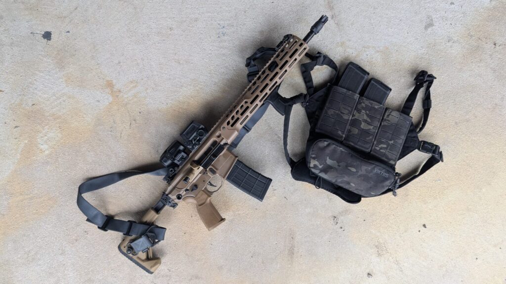 A SIG Sauer MCX-SPEAR LT rifle laid out next to a Viktos Taculus chest rig in Multicam Black.