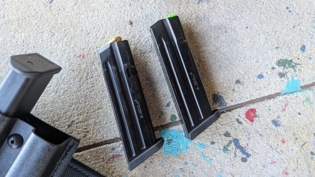 Two Mec-Gar Glock magazines resting on a concrete surface, showing the high-gloss finish and "Cal. 9mm" markings.
