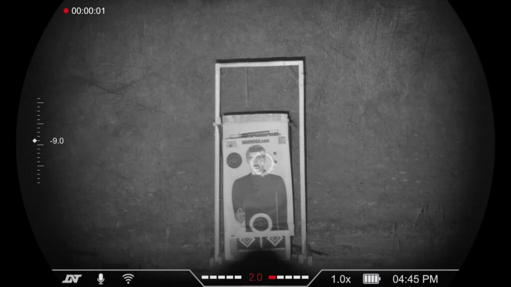 Grayscale night vision shot of a target frame in an open field, with visible distance and elevation markings on the left side of the HUD.