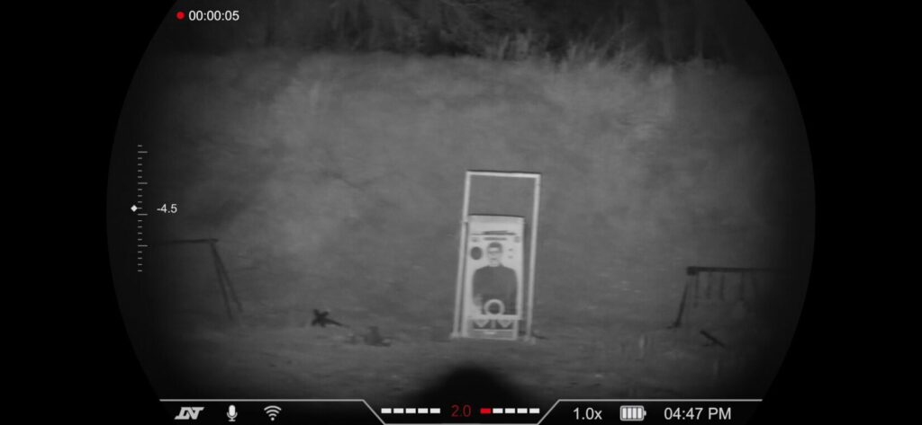 High-contrast night vision view of a paper shooting target featuring a human silhouette, seen through a 1.0x digital zoom.