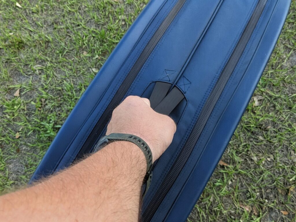 A hand gripping the main heavy-duty carry handle on the top of the blue Savior case.