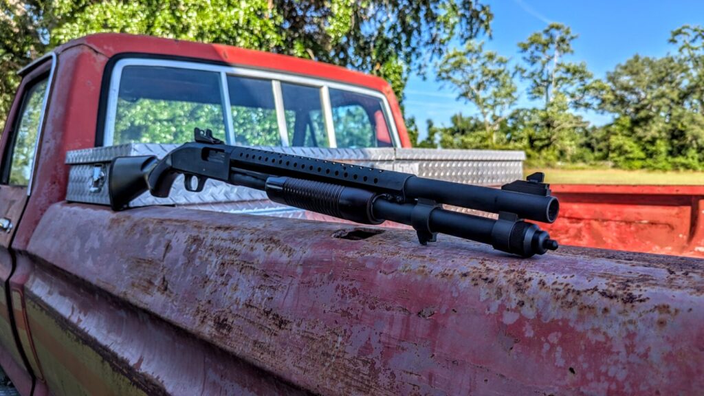 The Mossberg 590A1 shotgun resting along the side rail of a weathered, rusty red pickup truck bed.