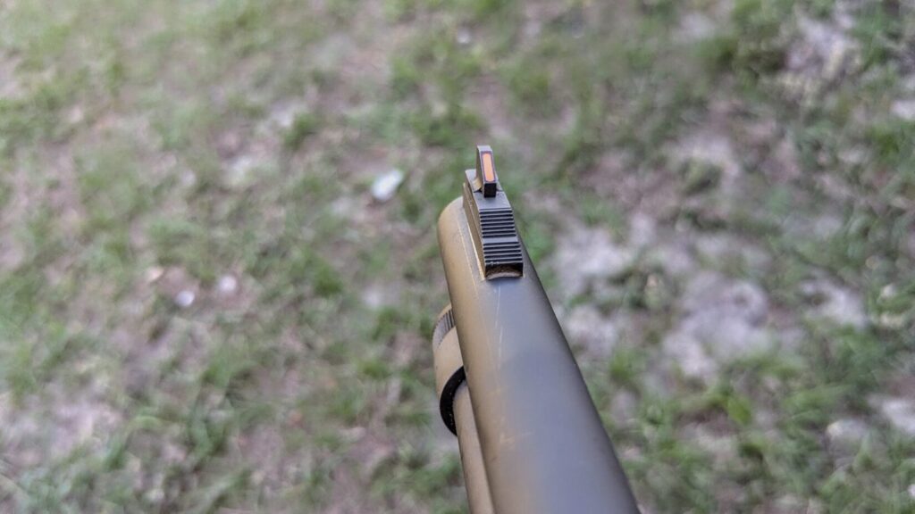 A view through the sights of the shotgun, showing the orange fiber-optic front sight post aligned at the end of the barrel.