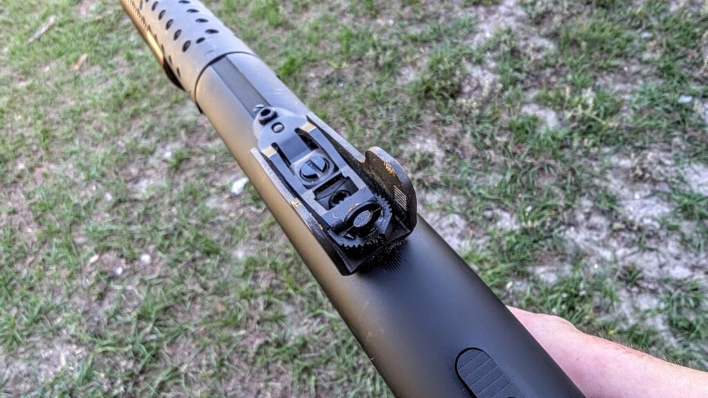 A first-person perspective looking down the length of the shotgun barrel, focusing on the adjustable ghost ring rear sight assembly.