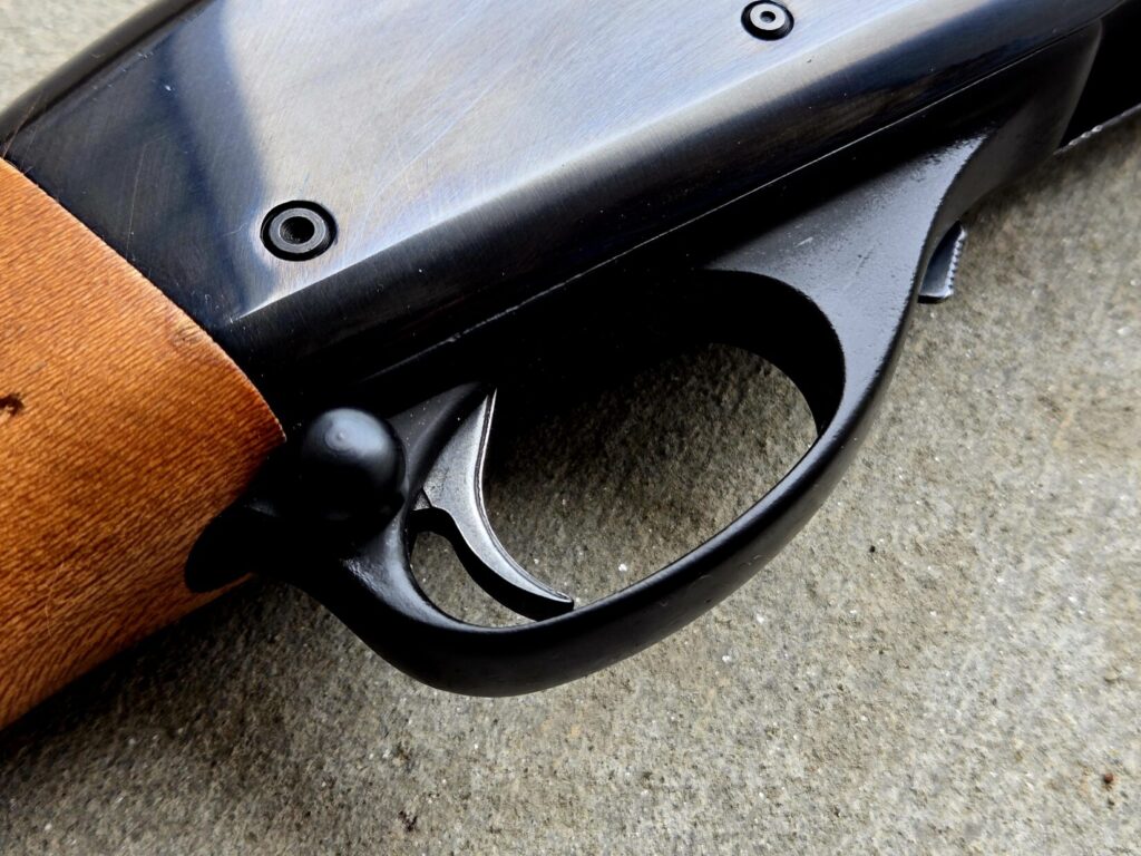 The trigger guard of a shotgun against a concrete backdrop