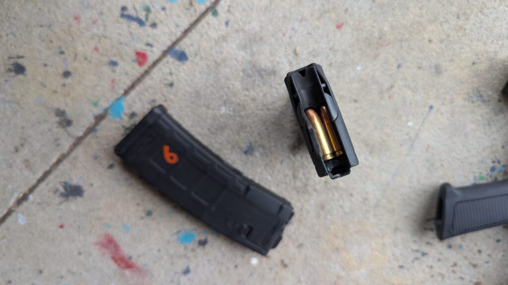 A close-up, top-down view of two rifle magazines; one is laying flat with an orange "9" and the other is standing upright, showing loaded brass cartridges.