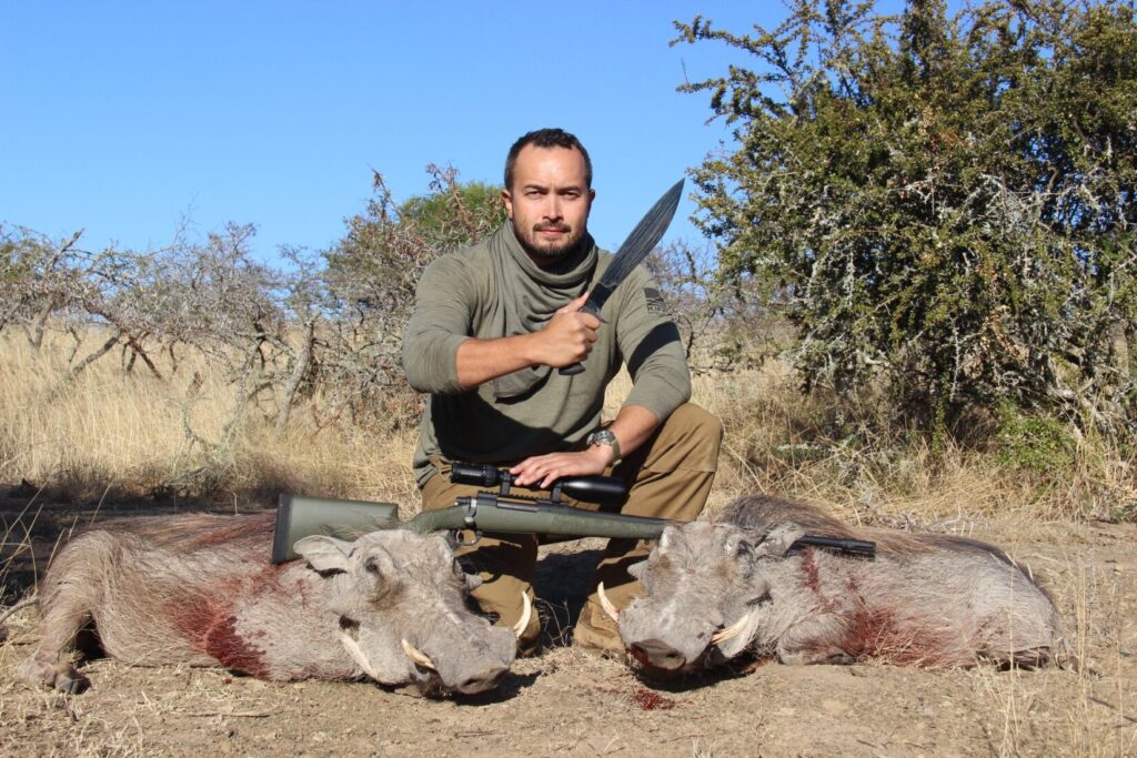 A man with a rifle and a large knife next to two warthogs in Africa
