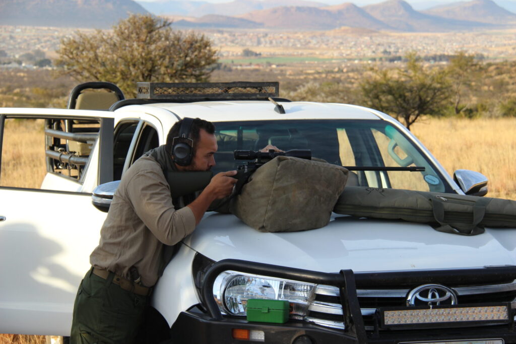 A man sighting in a rifle on the hood of a safari truck in Africa