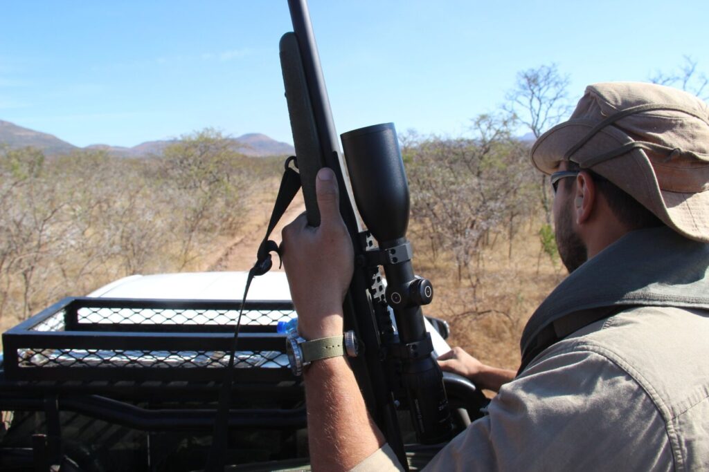 A man in a safari truck riding through Africa with a rifle