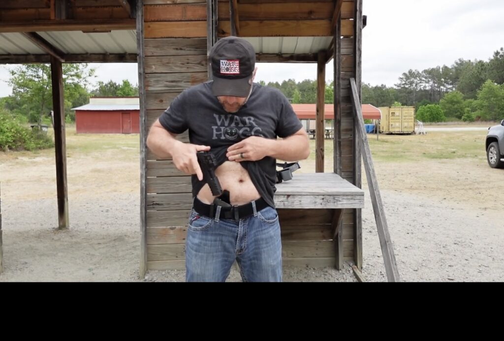 Rick Hogg founder War HOGG Tactical reholstering his pistol in an appendix concealed carry position