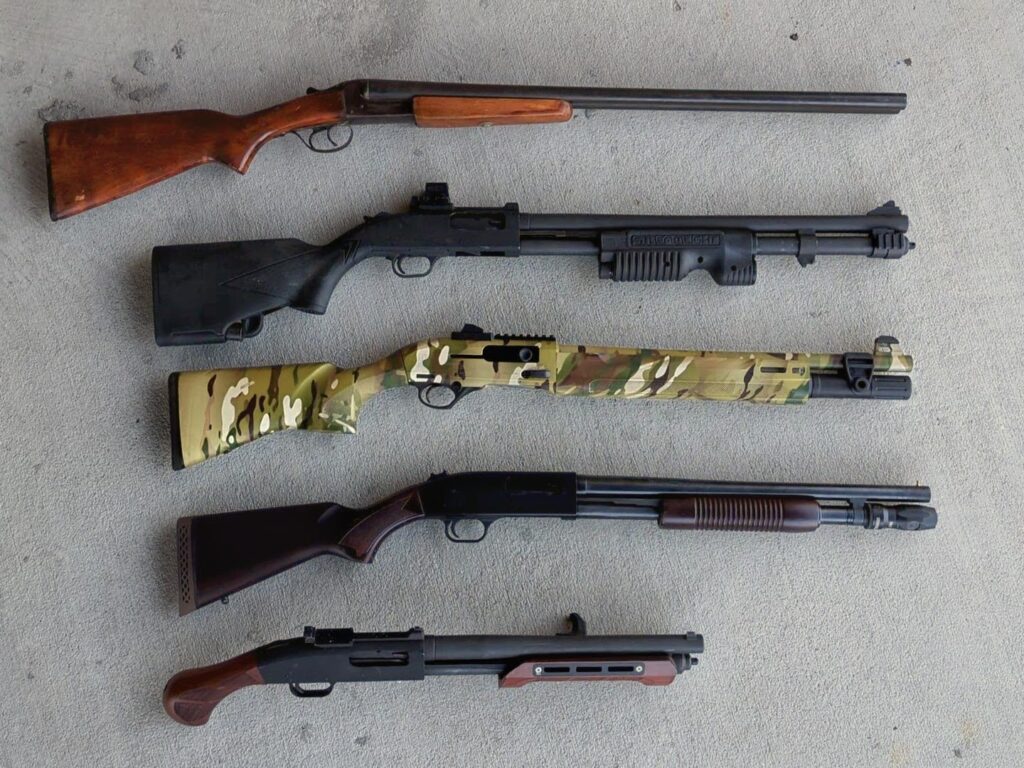 A top-down collection of five different shotguns, including a double-barrel, a camo-patterned semi-auto, and a short-barreled pump-action.