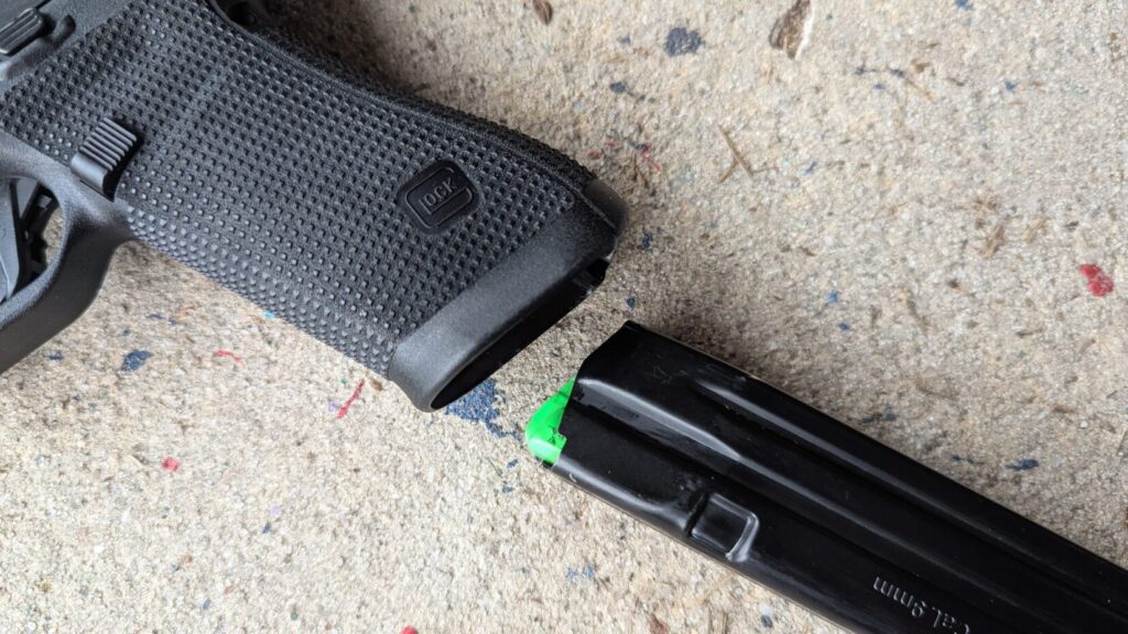 Close-up of a 9mm magazine with a bright green follower being aligned with the magwell of a black Glock pistol.