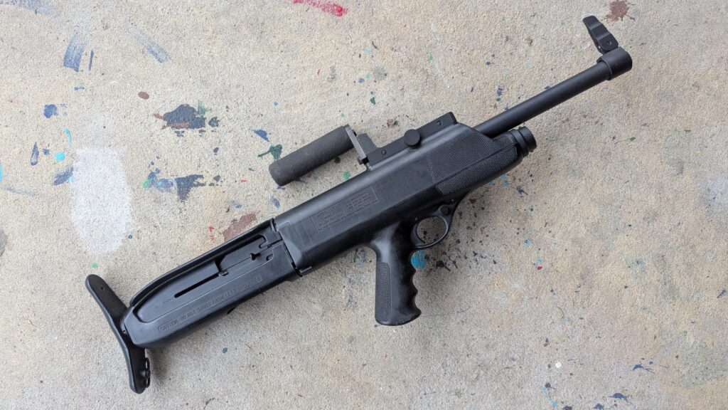 An overhead shot of a black High Standard Model 10B bullpup shotgun featuring a rotating carry handle and integrated flashlight.