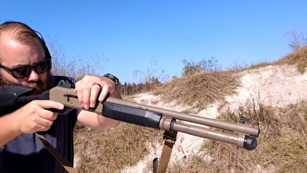 A close-up of a person operating a tan-colored semi-automatic shotgun, showing the action and tube extension.