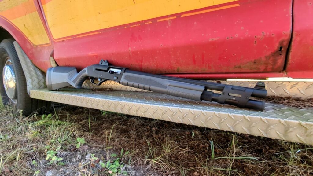 A grey semi-automatic Savage Renegauge shotgun rests on the diamond-plate step of a red and yellow vehicle.