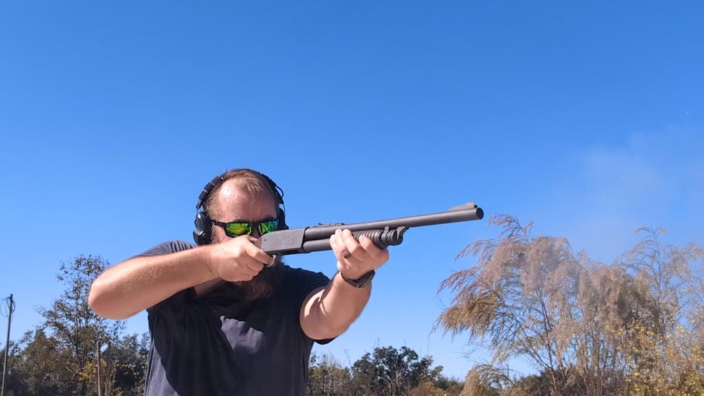 A person wearing bright green sunglasses aiming a classic pump-action shotgun with a wooden stock and long barrel.