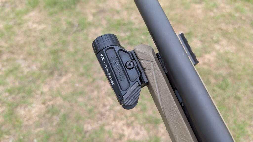 A close-up of a Holosun P.ID weapon light mounted to the tan forend of a shotgun.