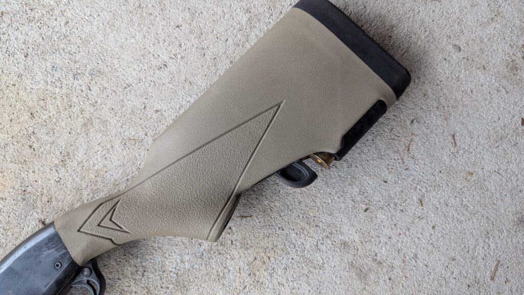 A detailed view of a tan tactical shotgun stock with an integrated shell holder containing a single brass shell.
