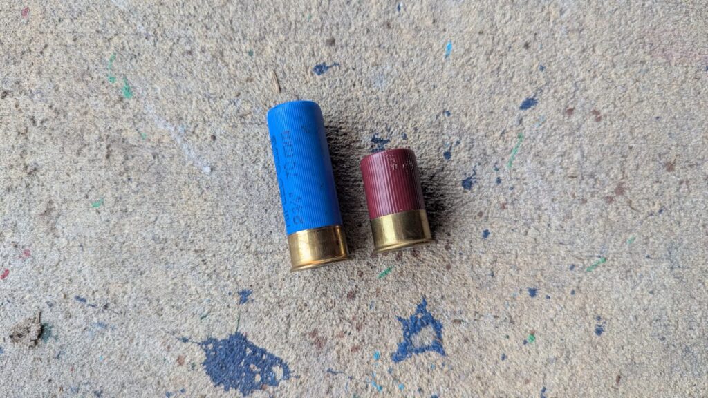 A comparison of two shotgun shells resting on a concrete floor: a standard blue 12-gauge rifled slug and a much shorter red shell.