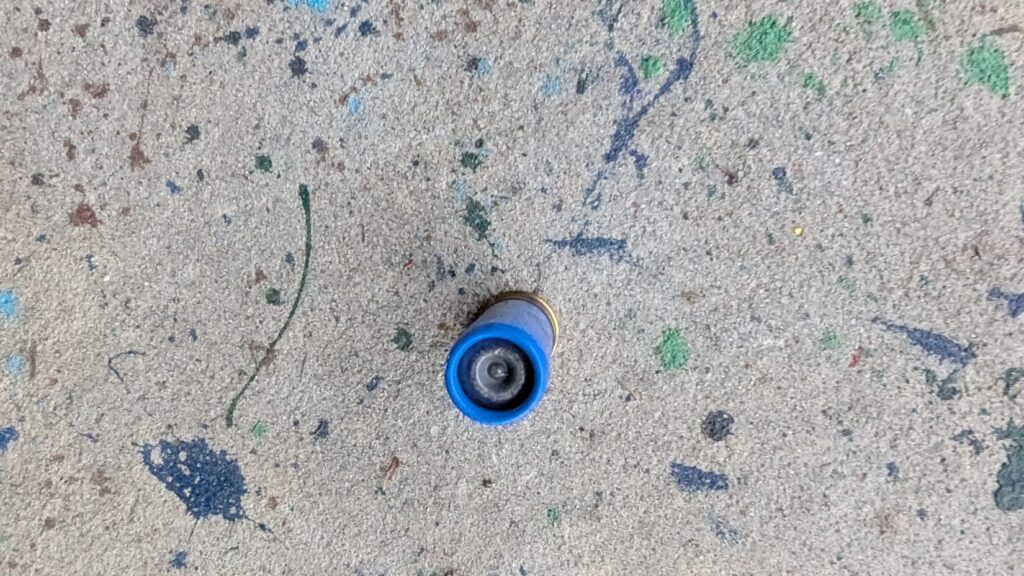 An overhead view looking directly down into the blue plastic hull of a shotgun shell on a concrete floor.