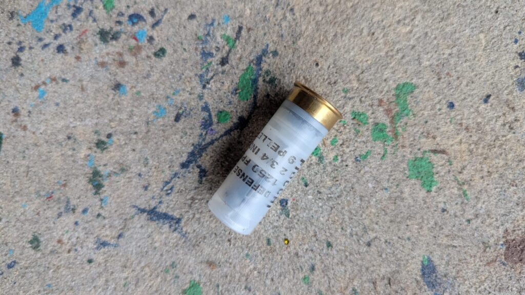 A single clear Fiocchi defense shotgun shell lying on a textured, multi-colored concrete floor.
