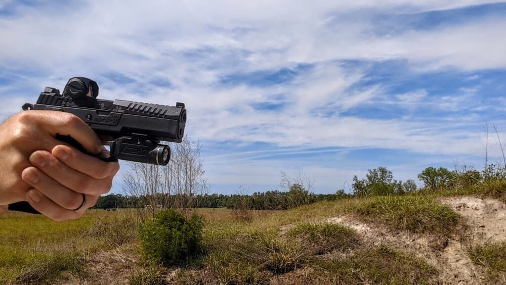 Profile view of a person aiming a CZ P-09 F Nocturne pistol equipped with a Steiner MPS-C red dot and a weapon light against a bright sky.
