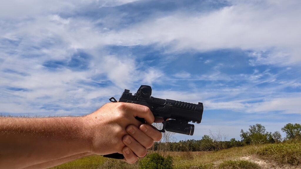 Profile view of a person aiming a CZ P-09 F Nocturne pistol equipped with a Steiner MPS-C red dot and a weapon light against a bright sky.